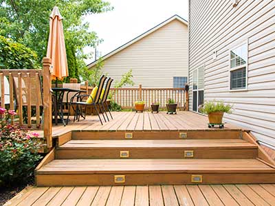 Side of a home with a large wooden deck with stairs and a table with chairs
