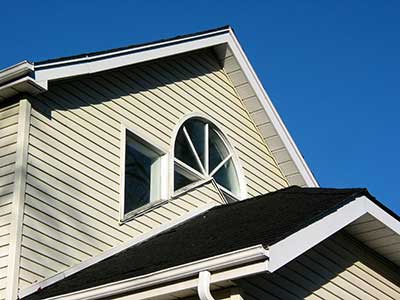 Close up of a home's exterior with beige siding and a black shingled roof